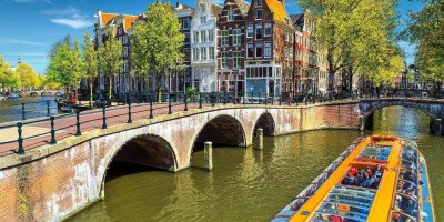 A tourist boat gliding through the Amsterdam canal, passing beneath bridges on a sunny day in Amsterdam, Netherlands.