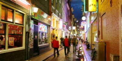 Bars and coffee shops on the street full of tourists at night in famous Red Light District in Amsterdam, Netherlands.