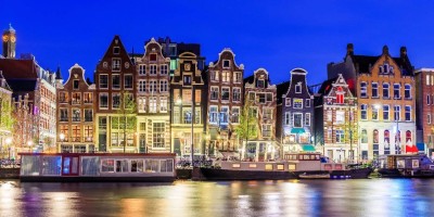 Amsterdam canal with boats and dutch houses at night.